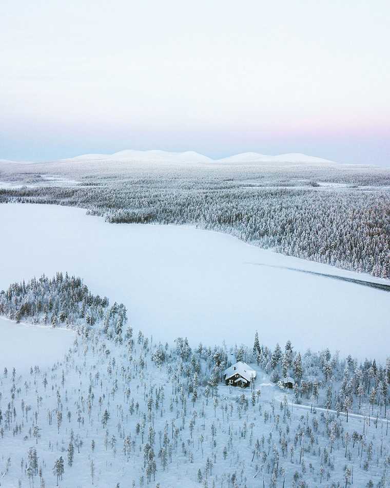 Snowbound forest and a frozen lake in northern Finland under a pale dawn sky