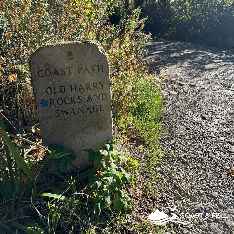 Stone coast path waymarker for Old Harry Rocks and Swanage beside a gravel track