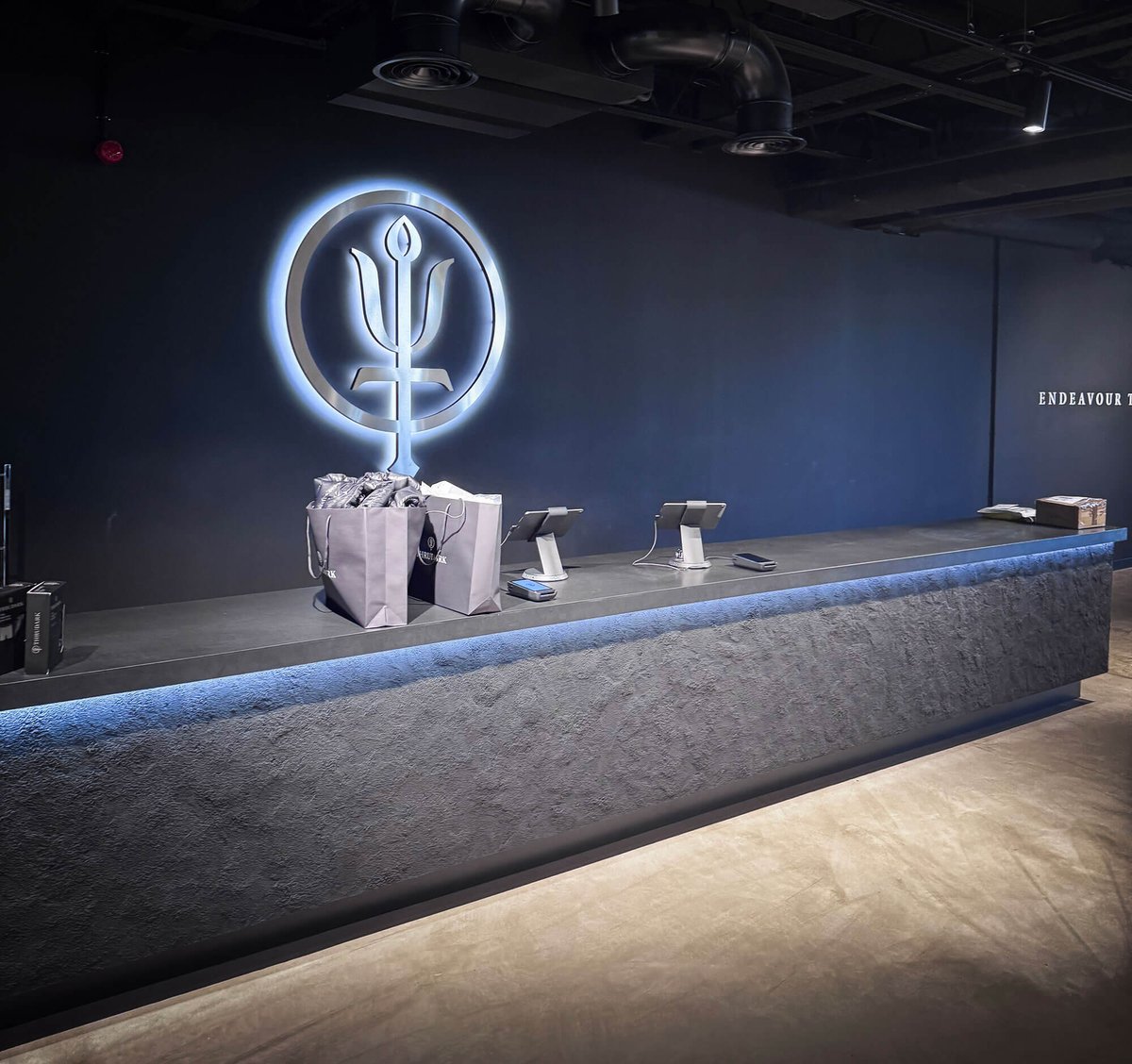The counter inside ThruDark's Sentinel House store in Poole, the backlit trident logo glowing on a dark wall