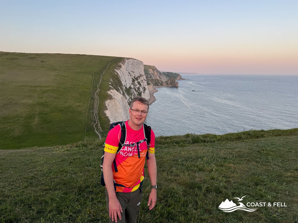 Shane in Breast Cancer Now vest on Hambury Tout at dusk with white chalk cliffs and pink sunset sky