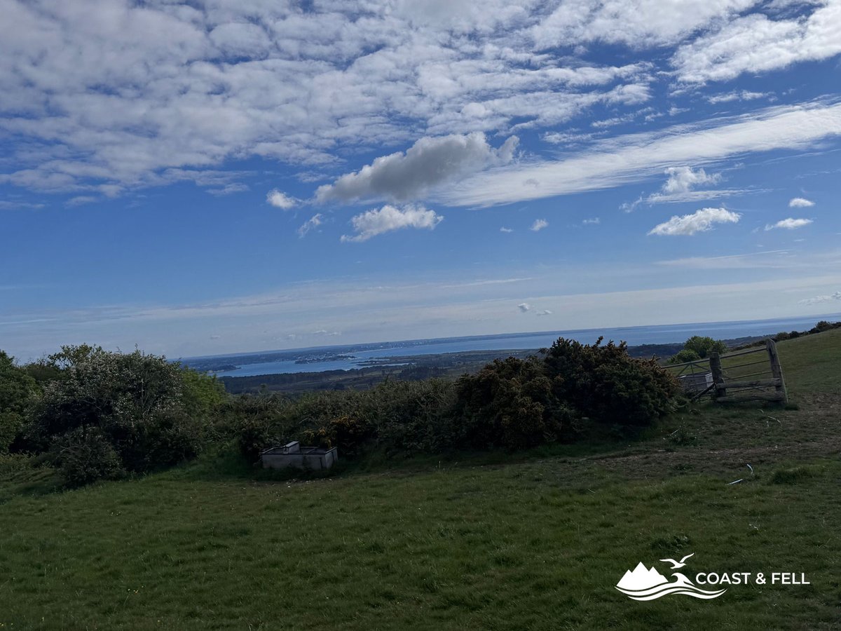 View north over Poole Harbour from Purbeck ridge high ground with blue sky clouds and a farm gate visible in foreground