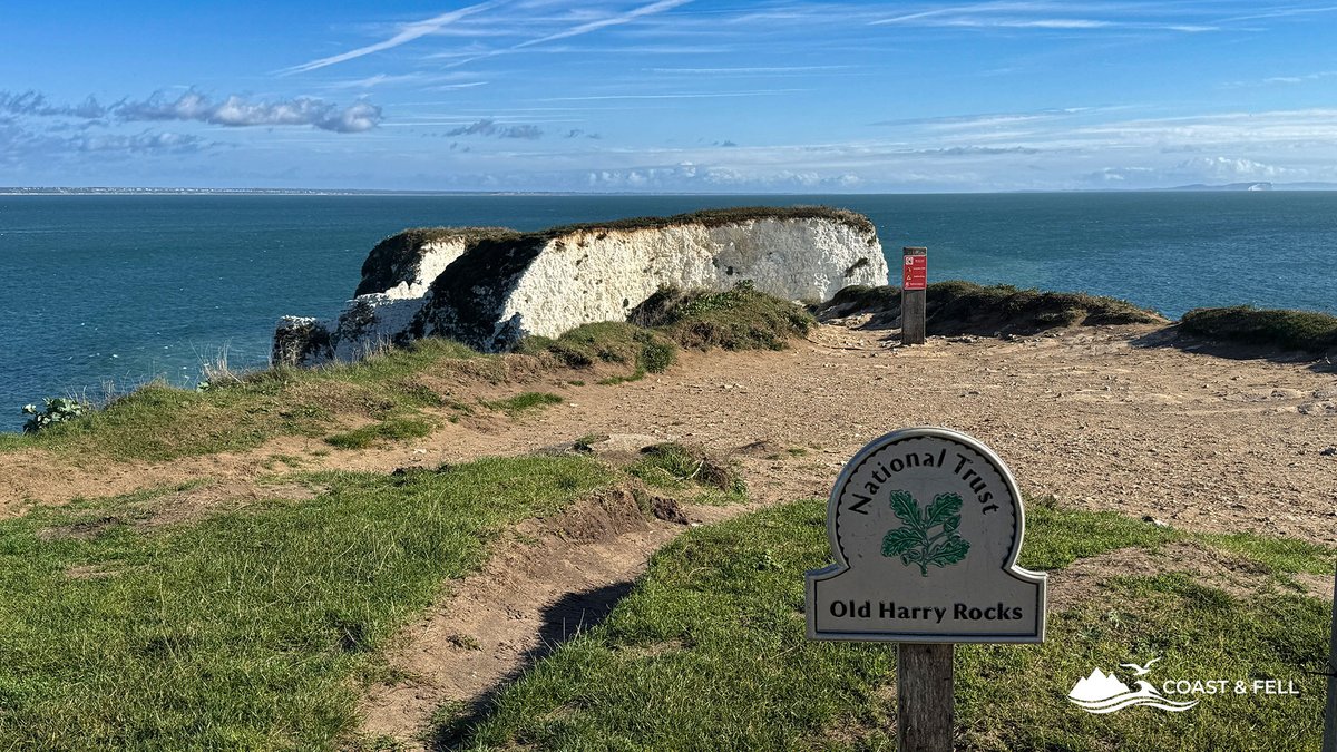 National Trust Old Harry Rocks sign on the clifftop path, with the white chalk headland and sea behind