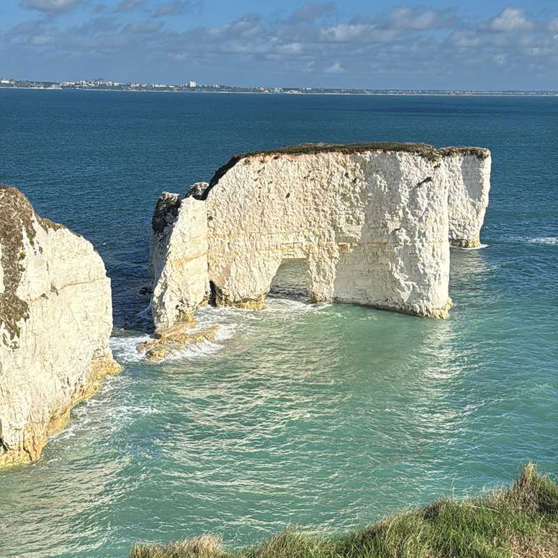 The chalk arch and stacks at Old Harry Rocks over turquoise water, Bournemouth on the horizon