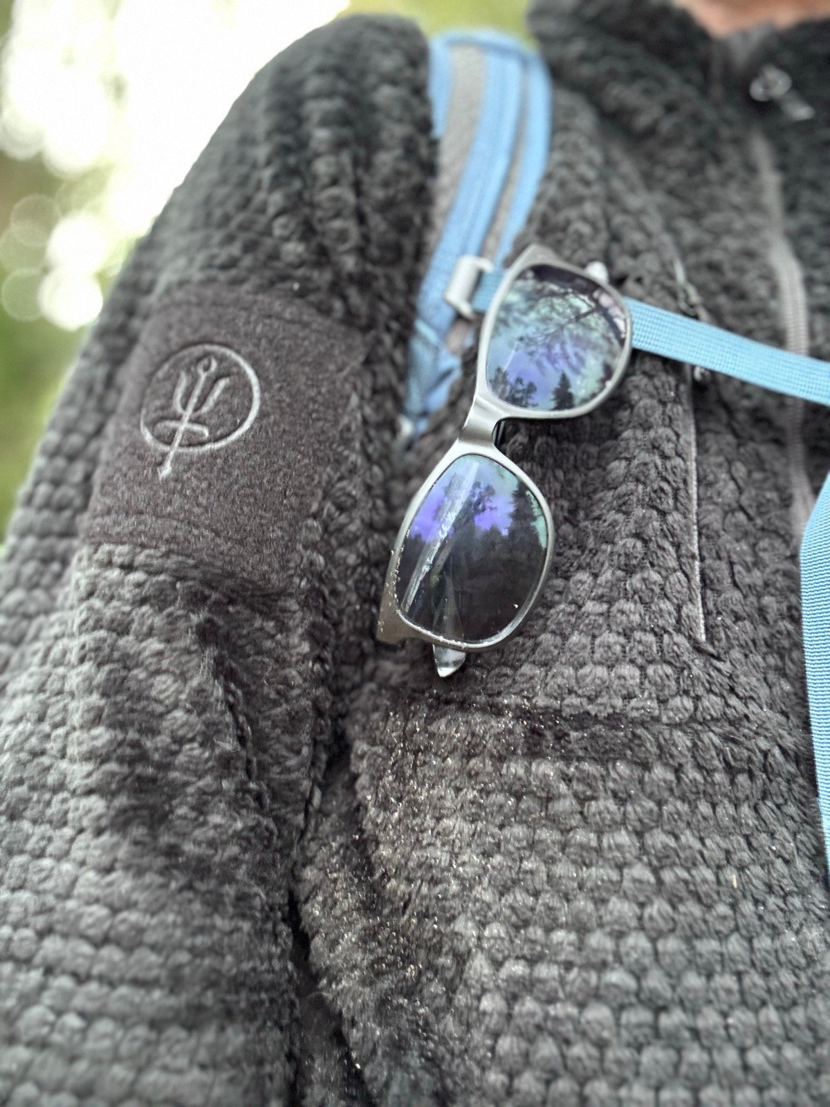 Close-up of the ThruDark Phalanx fleece, its grid-pile texture and the embroidered trident logo on the arm, with sunglasses hooked on the chest