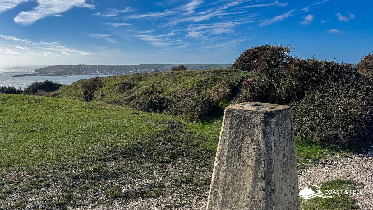 The trig pillar on Ballard Down, with the ridge path running on and Swanage bay glittering beyond