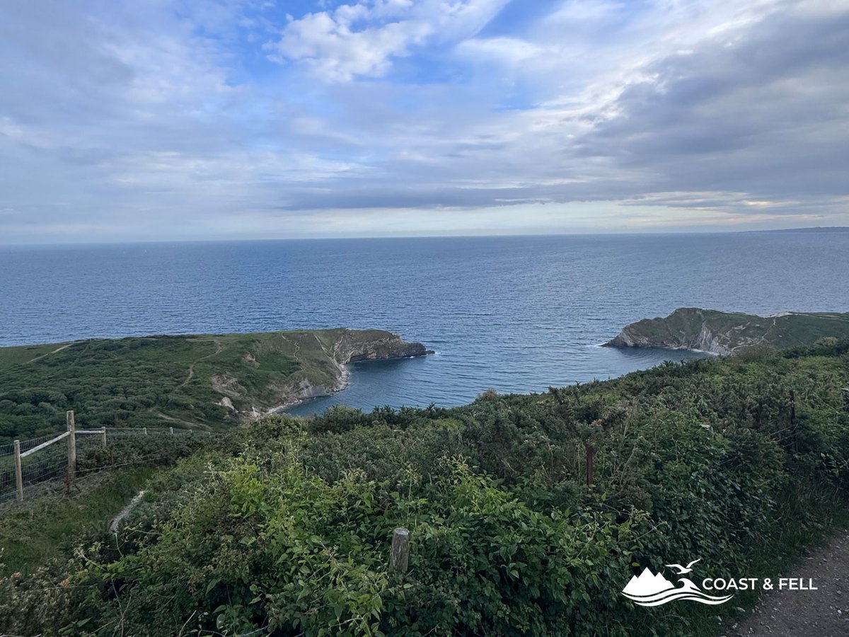 Lulworth Cove from coast path above showing circular bay enclosed by chalk and limestone headlands with sea beyond