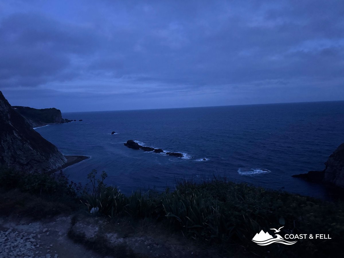 Jurassic Coast path at dusk with dark sea and rocky cliffs in deep blue light waves breaking on headland below