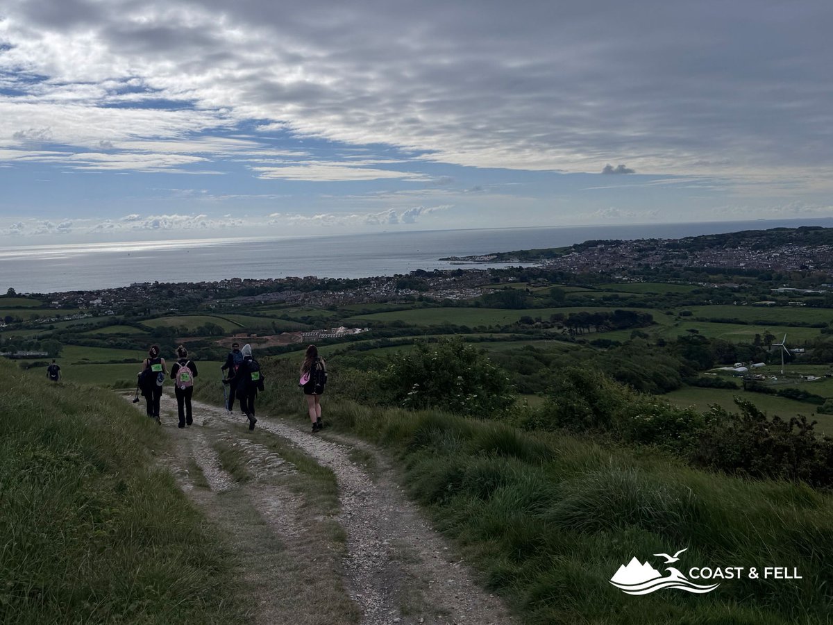 Participants descending chalk track toward Swanage with sea and coastline visible below overcast sky