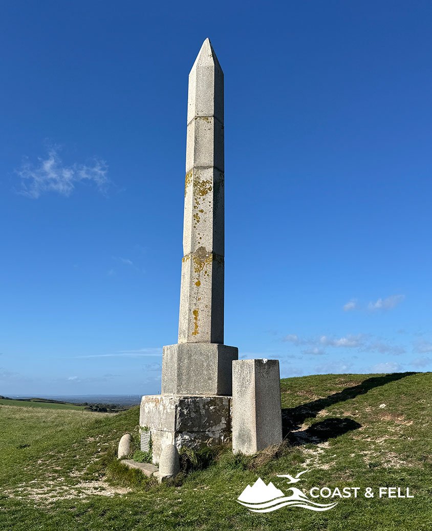 The Swanage Water Act Obelisk on Ballard Down, a hexagonal granite column on its stepped base, with the cracked original section mounted beside it