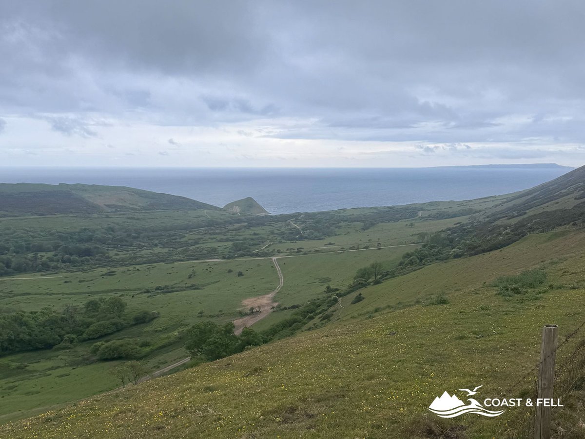 Green coastal valley on Jurassic Coast path rolling hills and headland and sea in distance under grey overcast sky