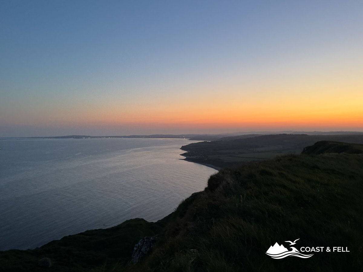 Sunset over Dorset coast orange glow silhouetted cliffs